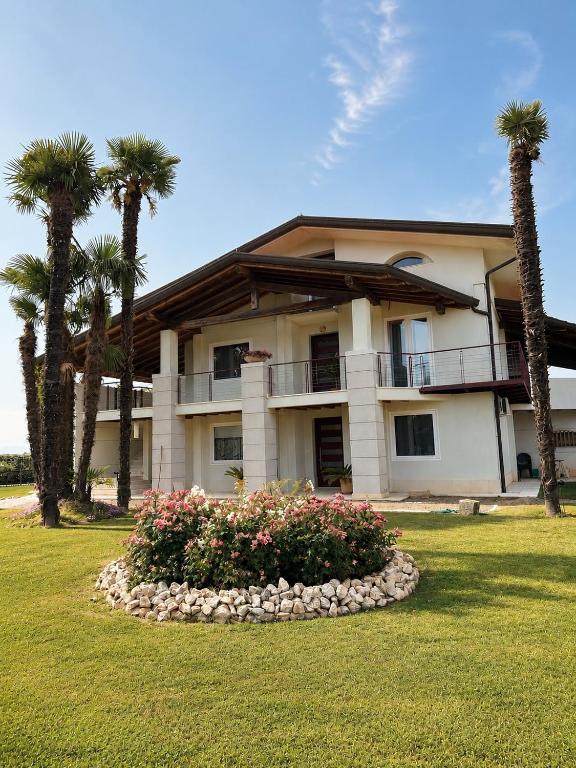 Villa Babilonia في Alvisopoli: منزل كبير به أشجار نخيل وشجيرة زهور