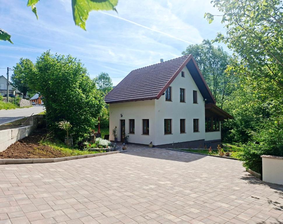 a white house with a black roof on a driveway at Kuća za odmor La Vi in Mrkopalj