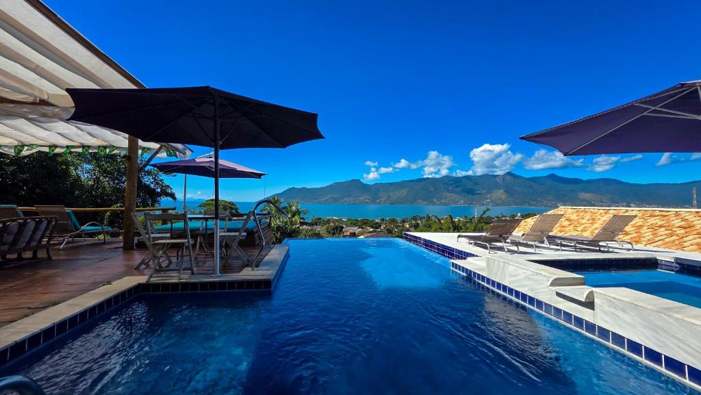 a swimming pool with a table and umbrellas at Studio Moderno com Vista pro mar com hidromassagem e churrasqueira privativas e Piscina aquecida na área comum in São Sebastião