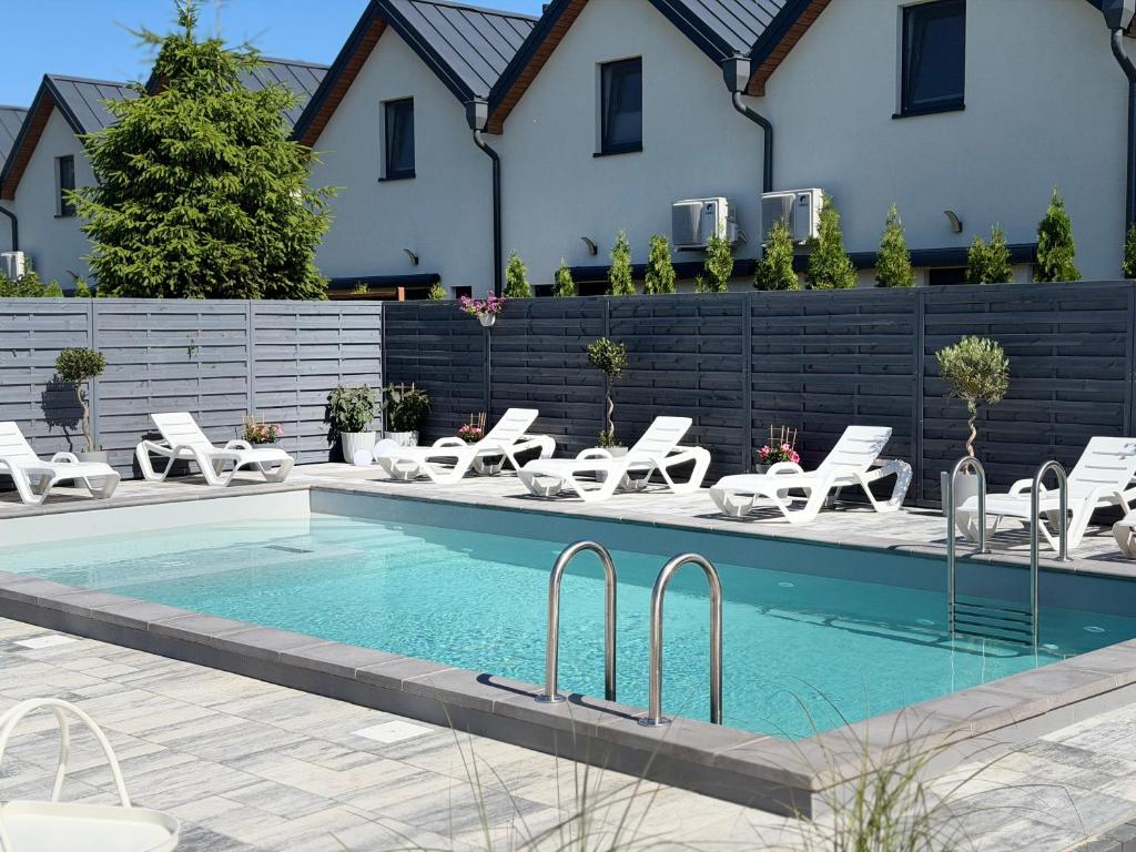 a swimming pool with lounge chairs next to a house at BalticMoon Rewal Domki z Podgrzewanym Basenem in Rewal