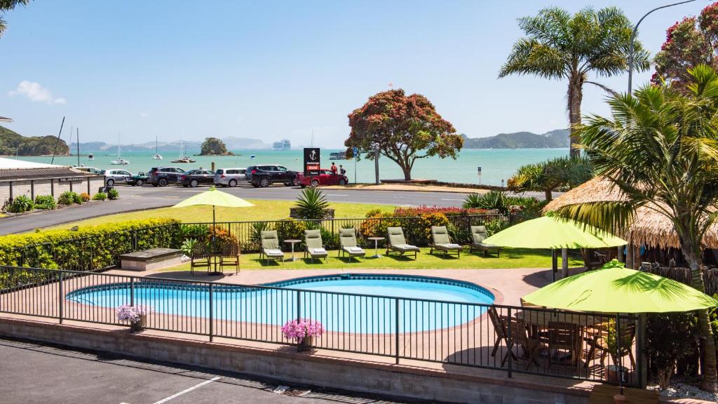 a pool with tables and chairs and umbrellas at Anchorage Motel in Paihia