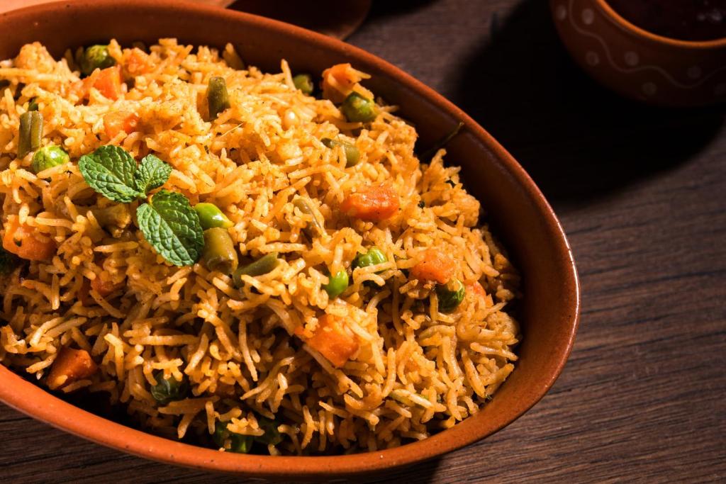 a bowl of rice with carrots and peas at Hotel O Nirsukh Palace in Navi Mumbai