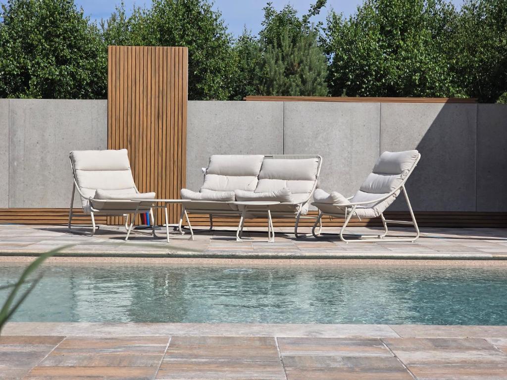 three lounge chairs and a pool next to a fence at Nadmorska Osada in Łeba