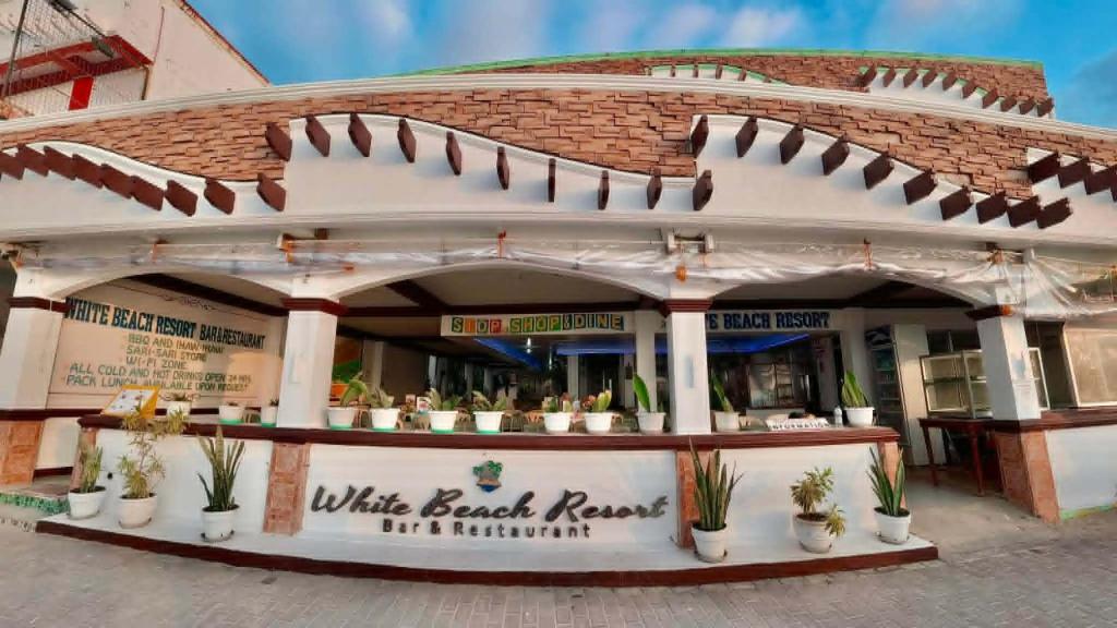 a white board house with potted plants in front of it at White Beach Resort Bar & Restaurant in Puerto Galera