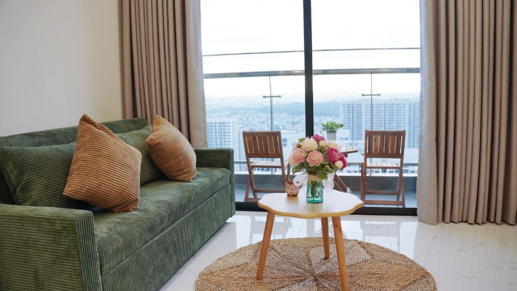 a living room with a green couch and a table with flowers at 2BR-2WC-Vinhomes Grand Park-Sunset View-VincomMeGaMall-WindyHomes in Long Bình
