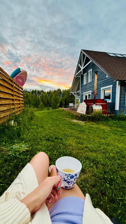 a woman laying in the grass with a cup of tea at Czaplowisko - skandynawskie domy na Kaszubach in Stare Czaple