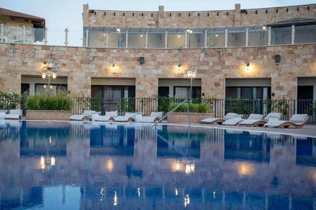 a swimming pool with white chairs and a building at Briaa Wellness Resort Hotel Gilboa - Adults Only in Maalé-Hagilbo‘a