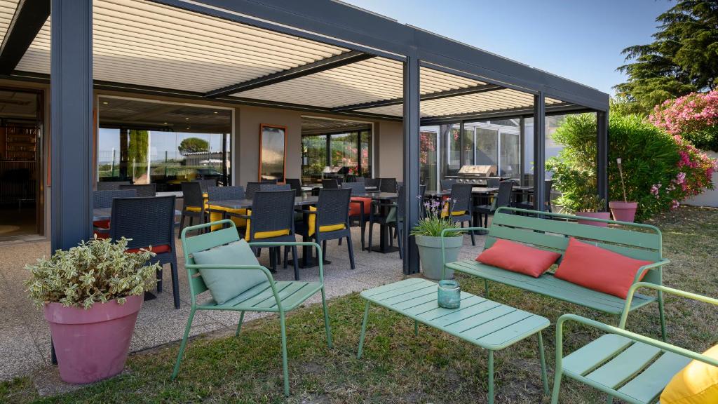 a patio with benches and tables and chairs and windows at Campanile NATURE - Bollene in Bollène
