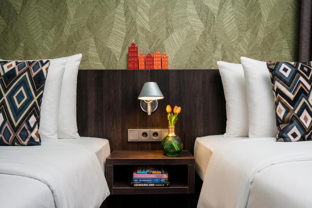 two beds with white pillows and a table with a lamp at Hotel Damsquare in Amsterdam