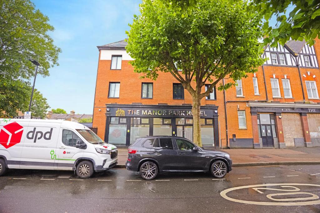 Zwei Autos parkten auf einem Parkplatz vor einem Gebäude. in der Unterkunft The Manor Park Hotel in London