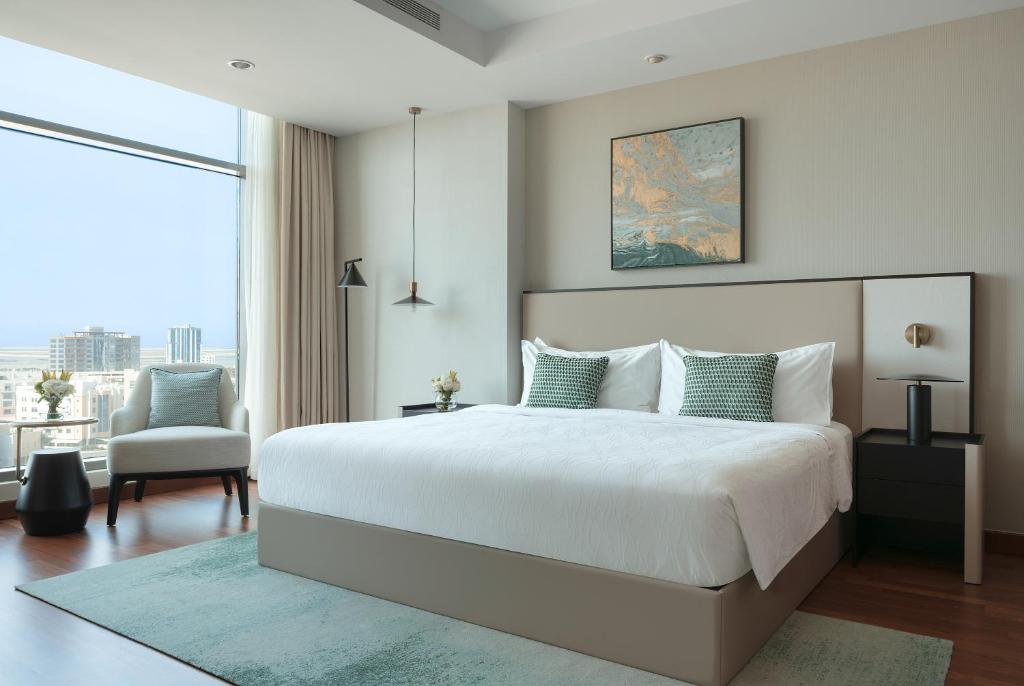 a white bedroom with a large bed and a chair at Fraser Suites Seef Bahrain in Manama