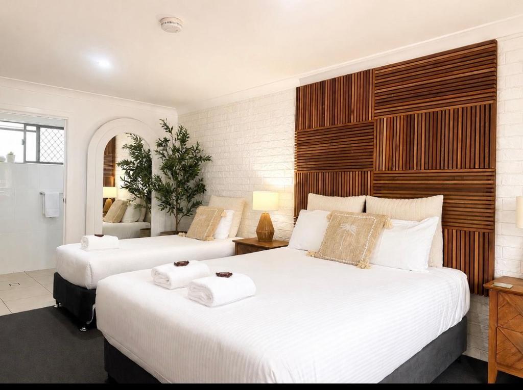two beds in a hotel room with white sheets at Beachmere Palms Motel in Beachmere