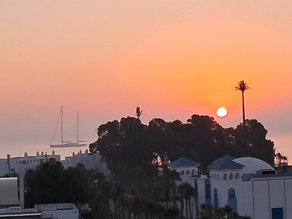a sunset over a city with a building and a palm tree at Appartement à m'diq in M'diq