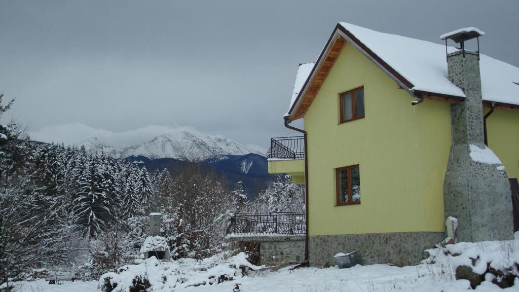una casa gialla nella neve con montagne sullo sfondo di Vila Eden a Porumbacu de Sus