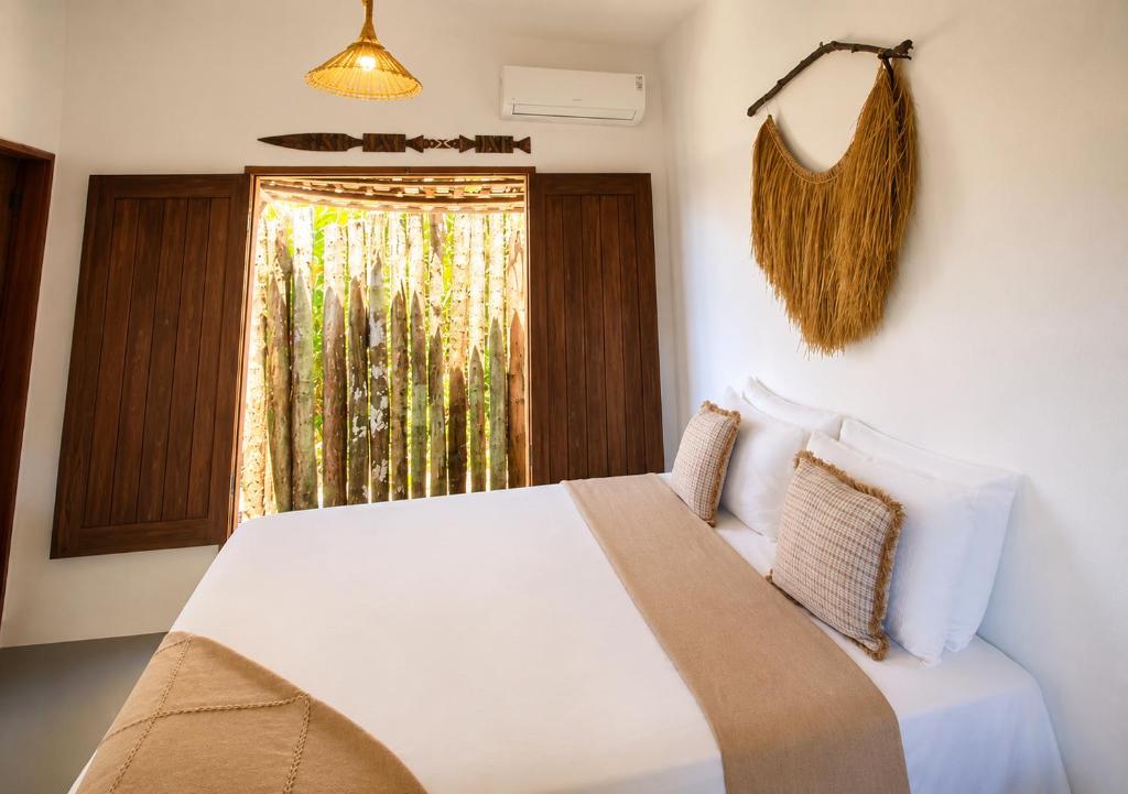 a bedroom with a white bed and a window at Lá na Chay Caraíva Refúgio tranquilo & experiência local in Caraíva