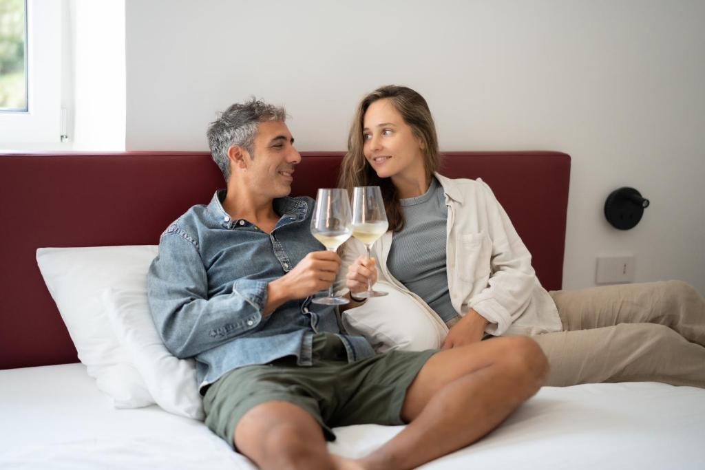 a man and woman sitting on a bed with glasses of wine at Guesthouse diWINE in Merano