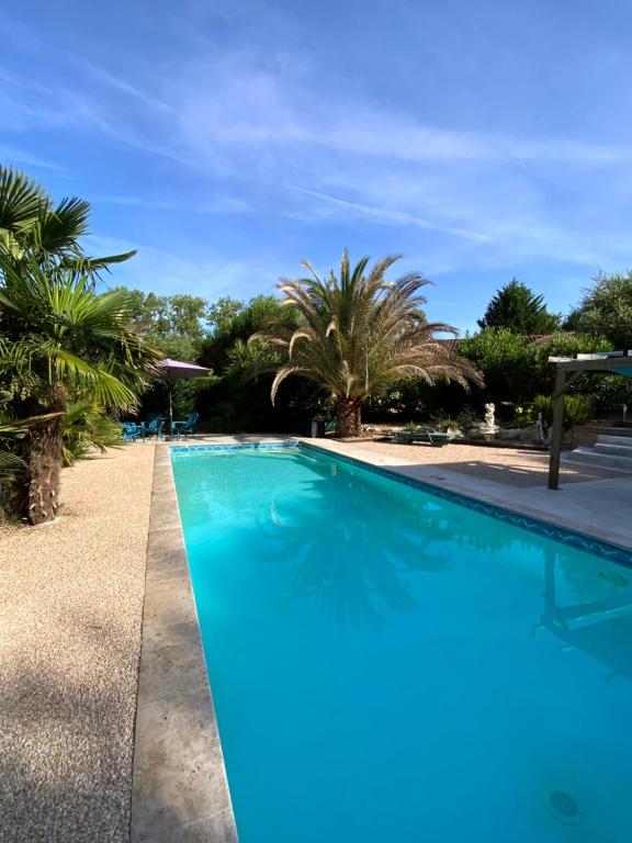 a blue swimming pool with palm trees in the background at Hacienda in Caumont