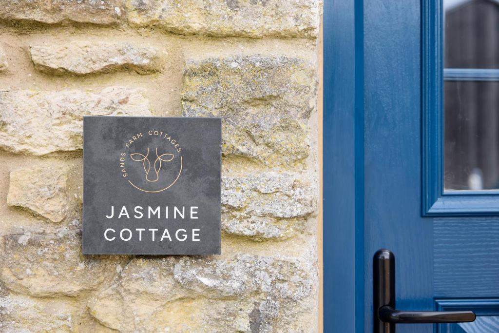 a sign on a stone wall next to a blue door at Jasmine Cottage - Sands Farm in Wilton