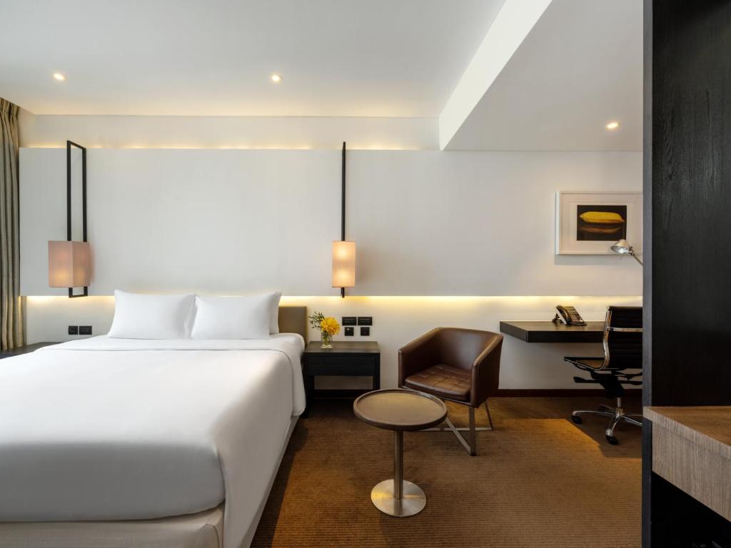 A modern guest room pairs a large bed with a compact desk and lounge chair.