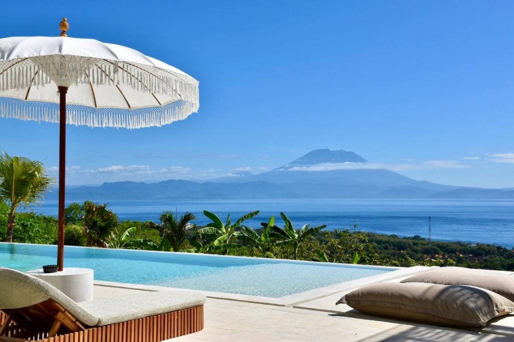 a swimming pool with an umbrella and a chair next to the ocean at Villa Kai Nusa Penida in Sampalan