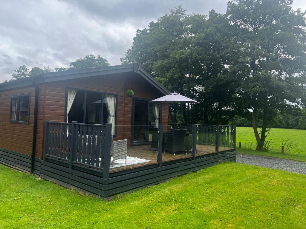 a small cabin with a deck and an umbrella at Crescent Lodge in Forton