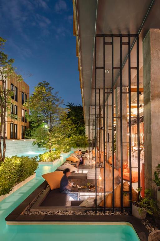 Poolside loungers line a narrow water channel beside a glazed hotel facade.