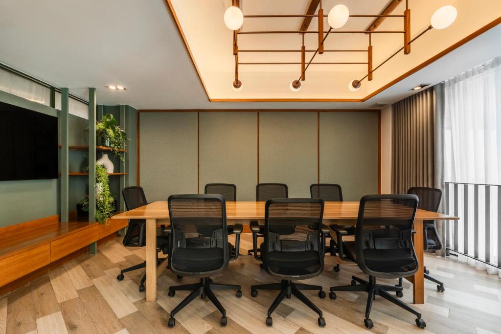 A bright conference room with a long table, rolling chairs and full-height curtained windows.
