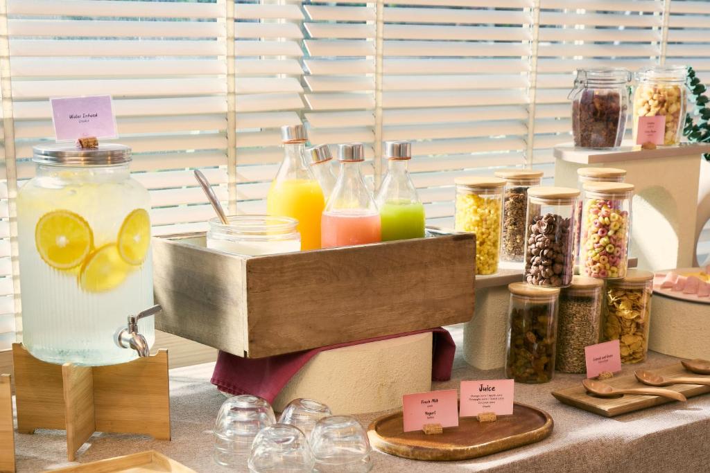 A self-serve drinks and toppings station with juices, infused water, cereals, and jars of add-ons.