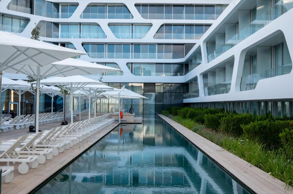 a building with a swimming pool with white chairs and umbrellas at The YACHT - By Fattal Limited Edition in Herzliya B
