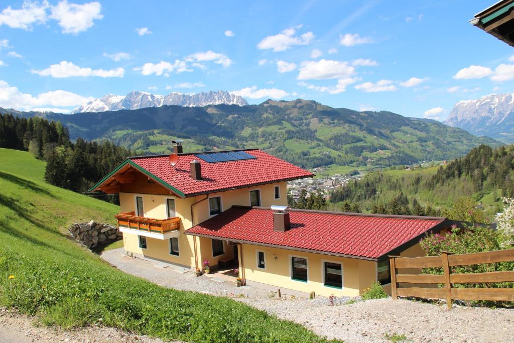 uma casa com um telhado vermelho com montanhas ao fundo em Holzlehenhof em Sankt Johann im Pongau