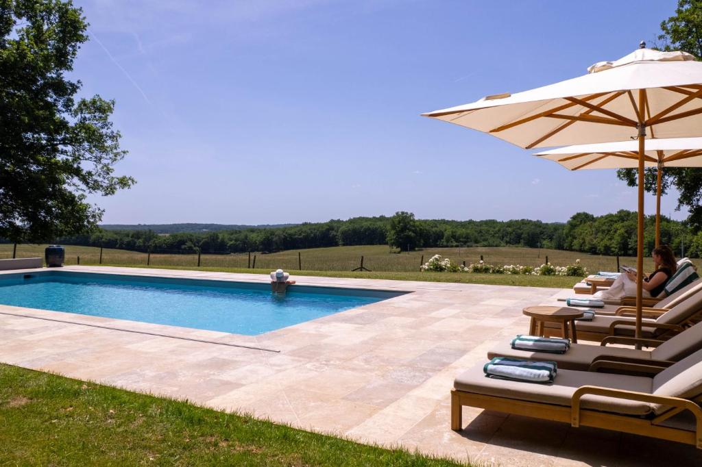 a couple sitting in chairs next to a pool with an umbrella at Villa de La Roussie in Saint-Sulpice-de-Mareuil