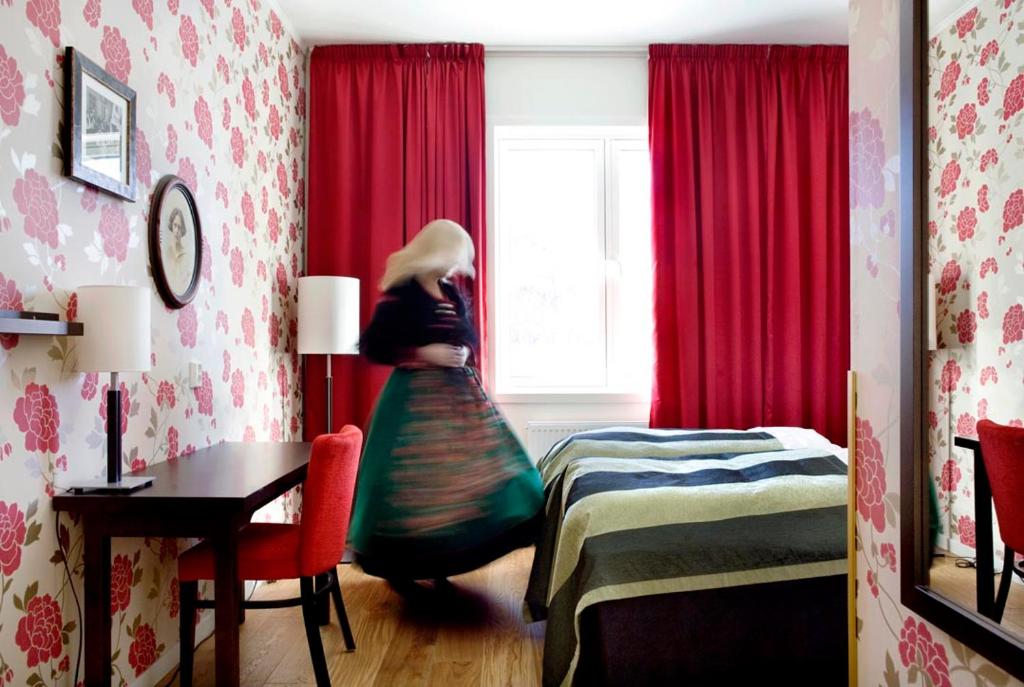 a woman in a room with a bed and a window at Søstrene Storaas hotell in Bolkesjø