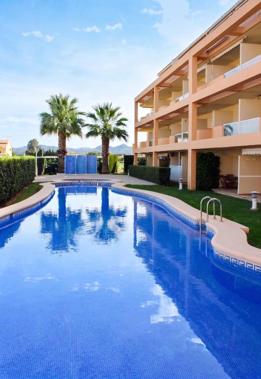 a swimming pool in front of a building with palm trees at Cozy apartment in Dénia, 40 m² with shared pool in Denia