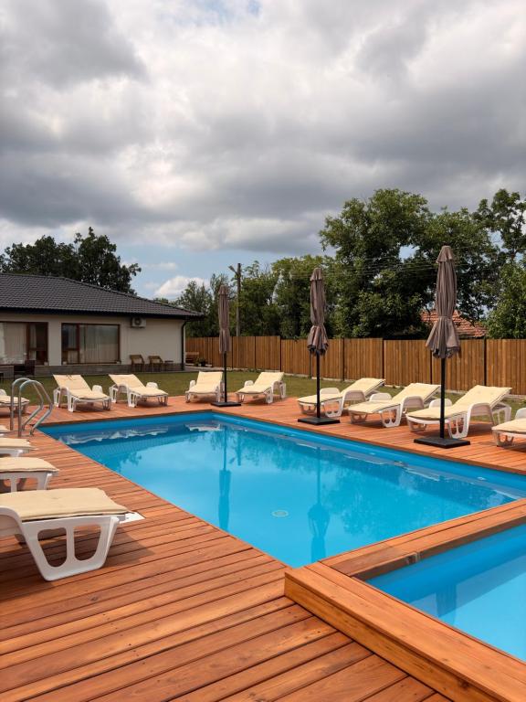 a pool with chairs and umbrellas on a wooden deck at Братановите Къщи in Dŭbravka