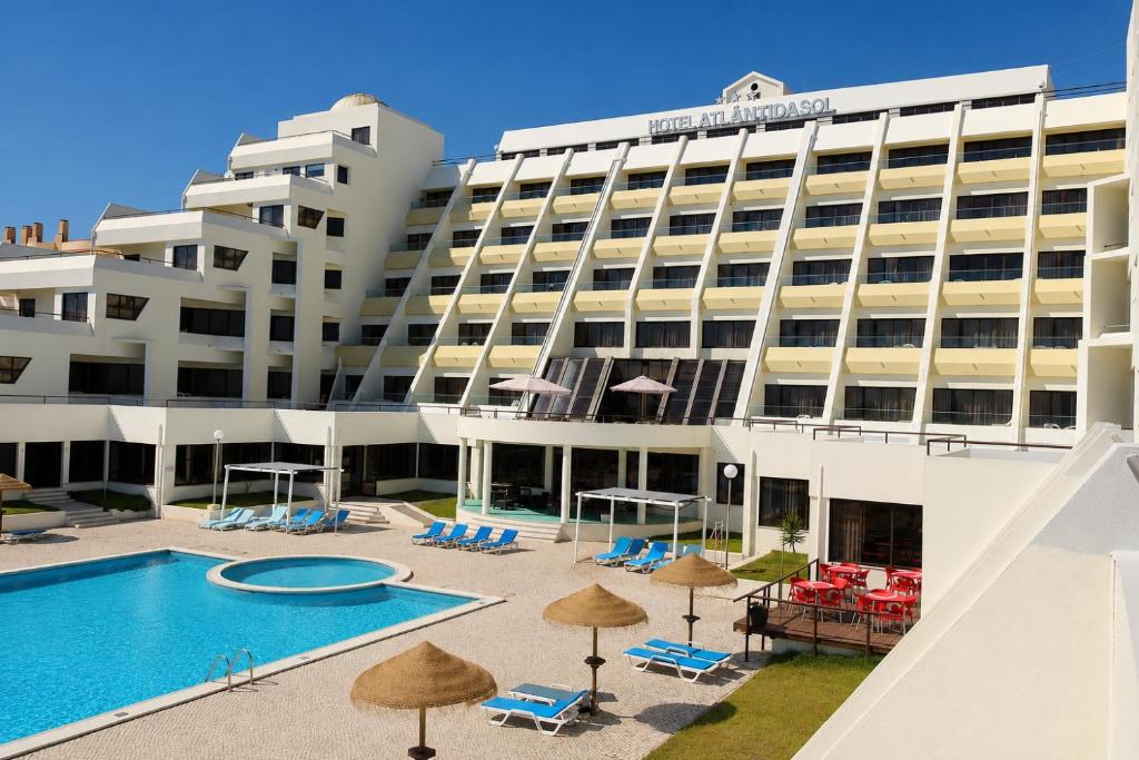 a hotel with a pool and chairs and umbrellas at Hotel Atlantida Sol in Figueira da Foz