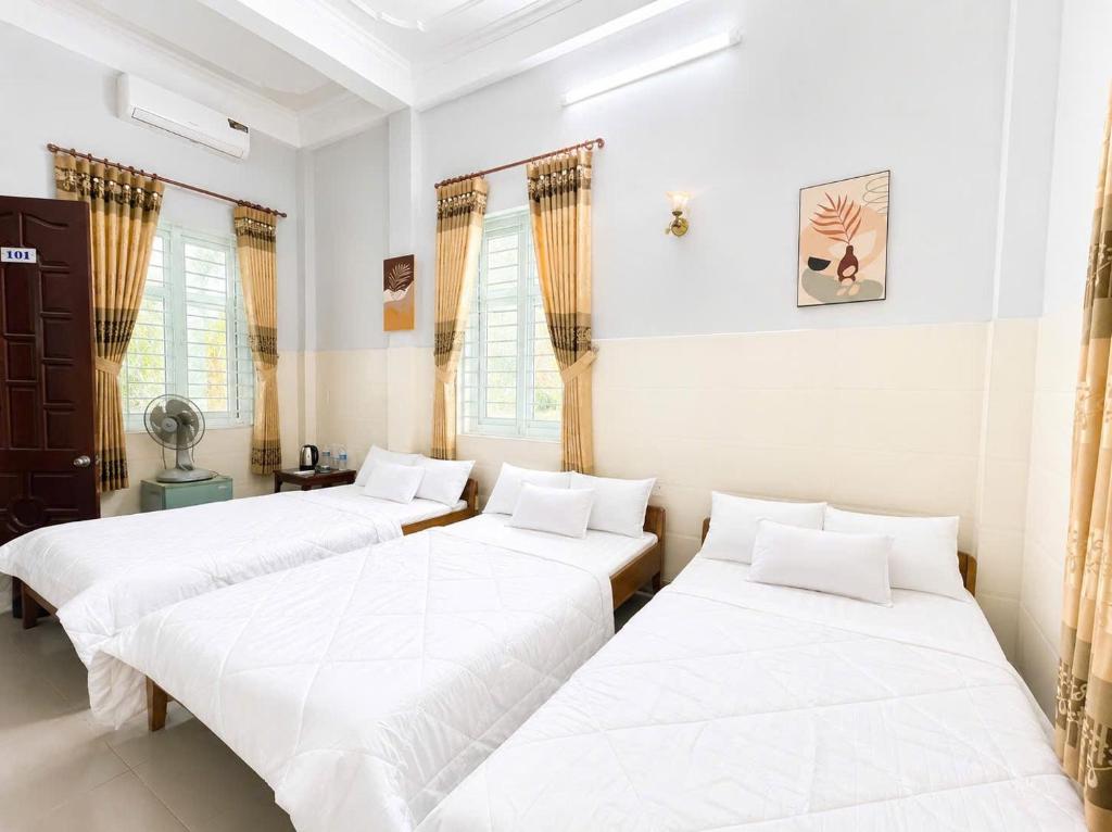 three beds in a room with white walls and windows at ĐAN MY Motel in Dong Hoi