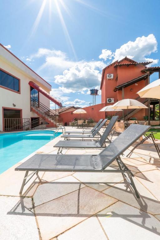 a group of lounge chairs and umbrellas next to a swimming pool at Villa Zen Pirenópolis Conforto e Bem-Estar in Pirenópolis