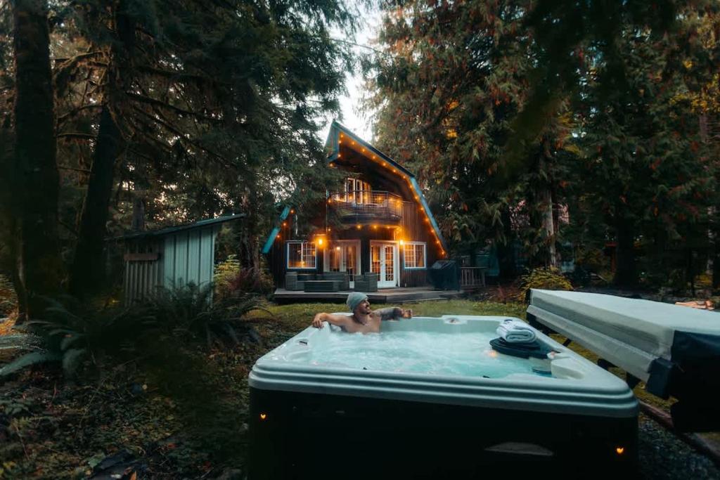 a man in a hot tub in front of a house at Alpine Lodge in Glacier