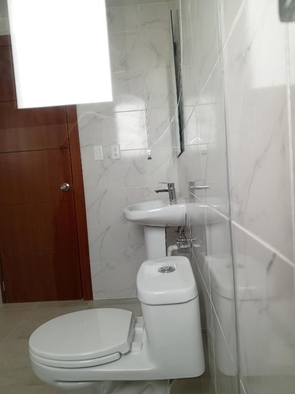 a white bathroom with a toilet and a sink at Apartamentos Latacunga in Latacunga