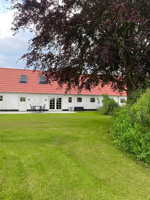 a white building with a red roof and a green yard at Uggerhøjvej Gårdhygge in Hjørring