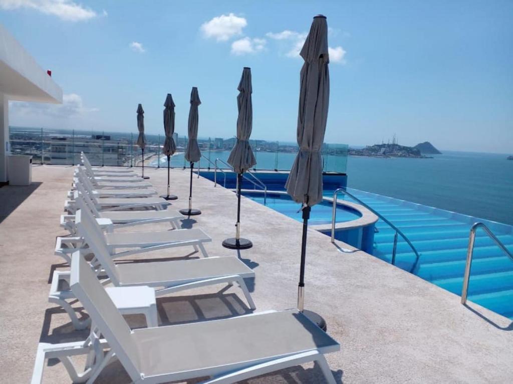 a row of lounge chairs and umbrellas on the edge of a pool at Departamento en el malecón, Torre Central 102 in Mazatlán