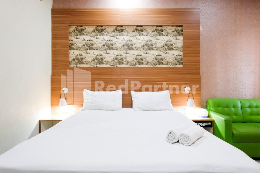 a bedroom with a white bed and a green chair at As Waru Hotel RedPartner in Palang-Putih