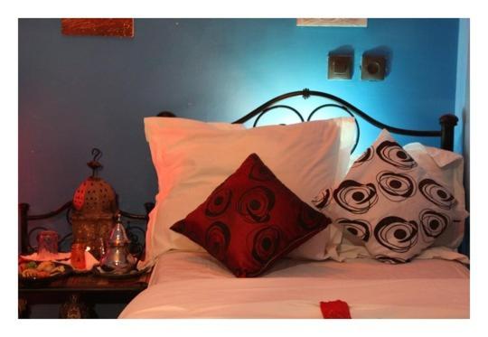 a bed with red and white pillows and a blue wall at Karim Sahara in Zagora