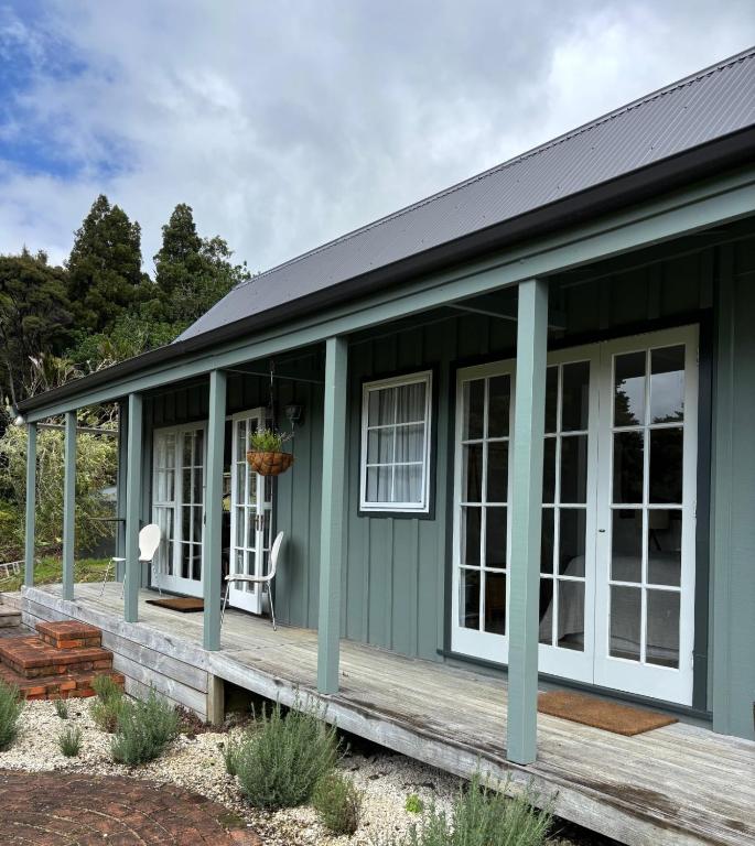 a green house with white windows and a porch at Lulu's Cottage by Native Forest in Waimauku
