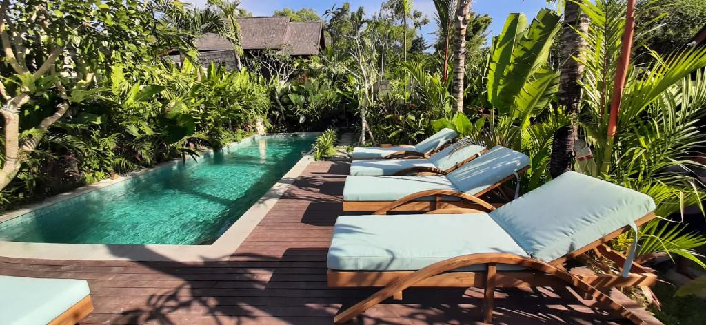 a row of chaise lounge chairs next to a swimming pool at The Woods Uluwatu in Uluwatu