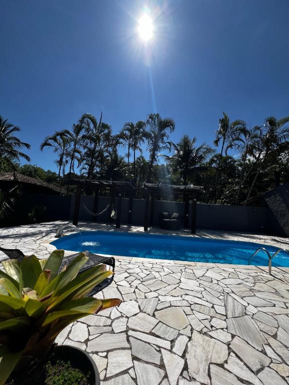 a swimming pool with a stone patio and palm trees at Chalé em Maresias - Quintal Privativo - Pet Friendly 4 Hóspedes in Maresias