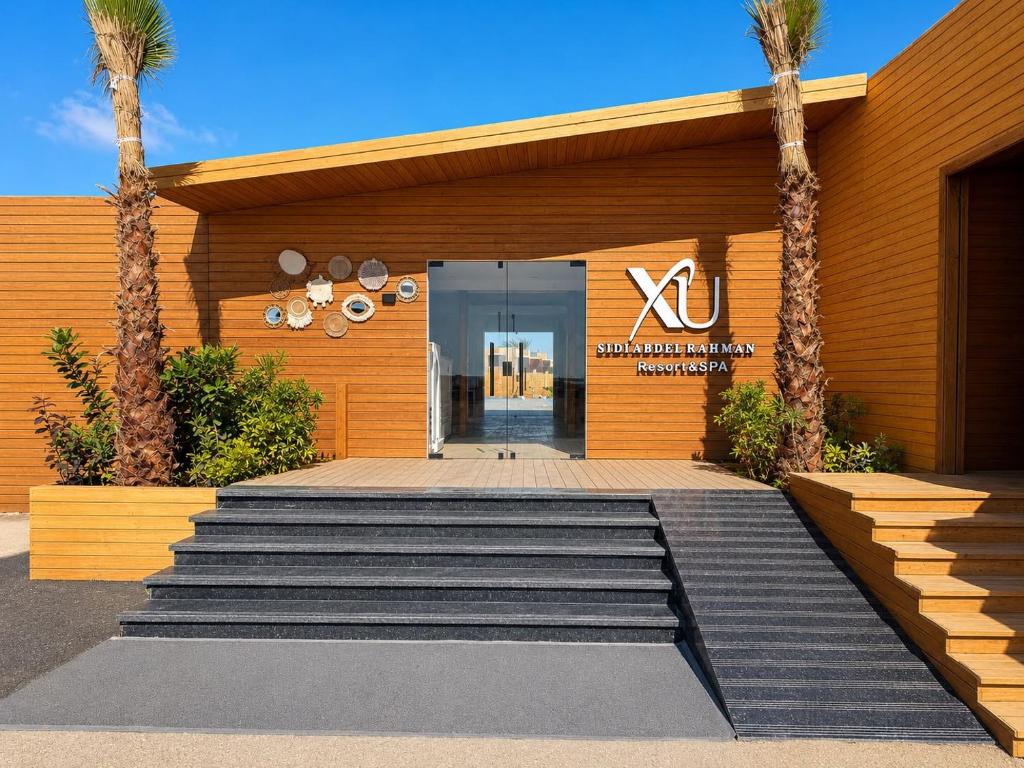a building with a lobby with palm trees in front at XU Sidi Abdel Rahman Resort & Spa in El Alamein