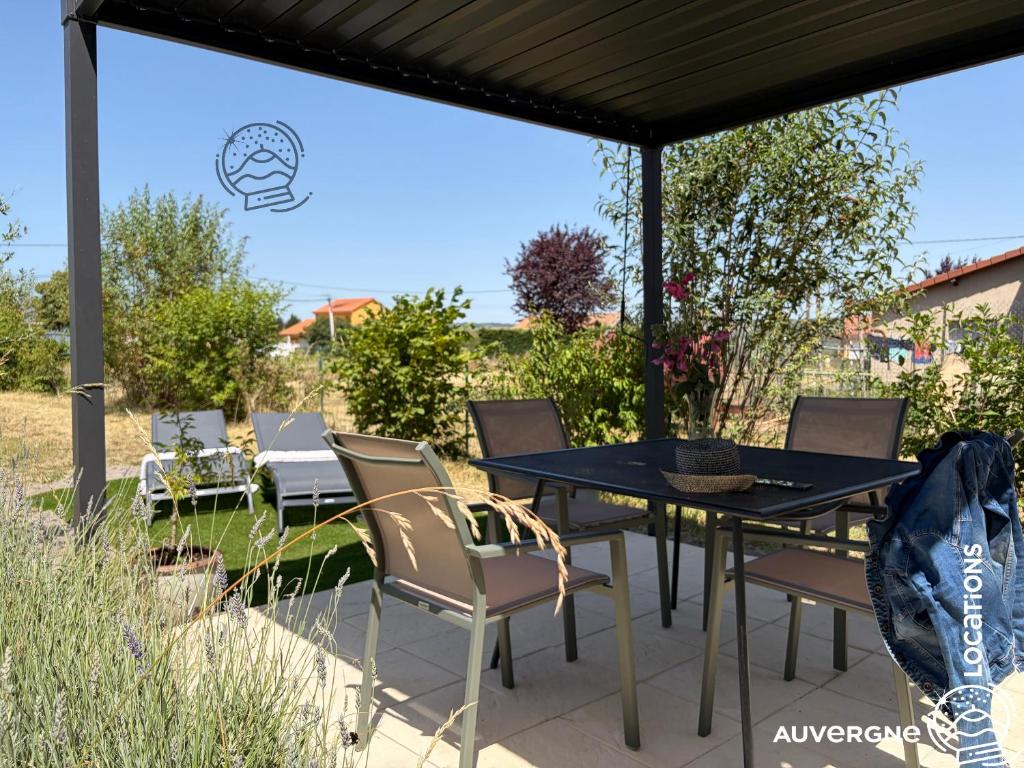 a patio with a table and chairs under a roof at Le Chardonneret du Sancy in Montaigut-le-Blanc