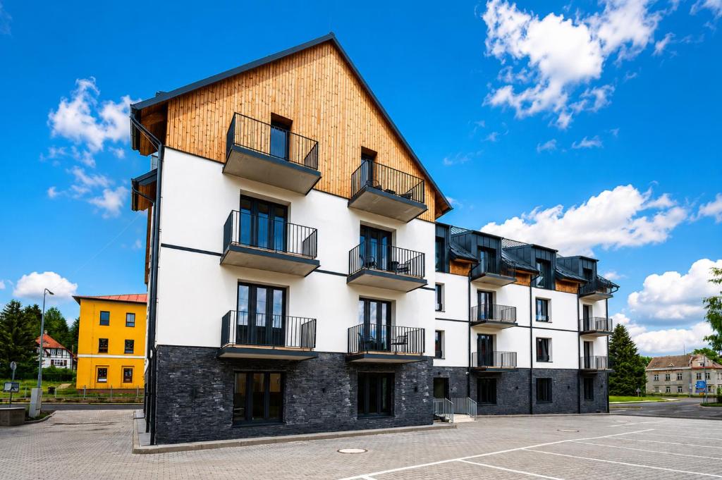 a white building with black balconies on a parking lot at Apartmány Perninský Dvůr in Pernink