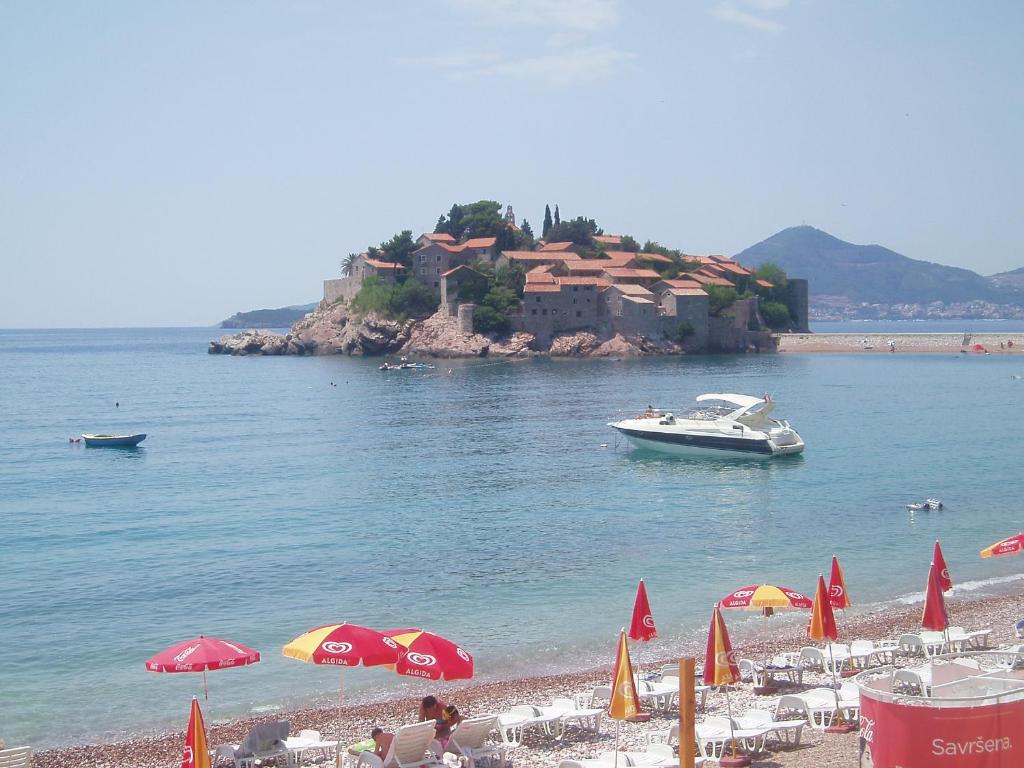 a beach with umbrellas and a boat in the water at Apartments Secret Garden in Sveti Stefan